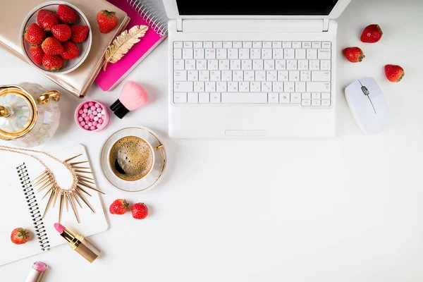 Feminine home workplace. Home office desk with laptop, notebook, fresh strawberries, cosmetics, woman accessories and coffee cup on white background. Flat lay, top view