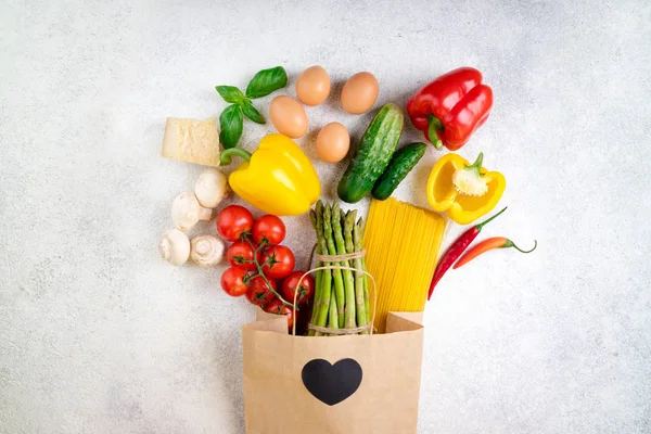 Healthy food background. Healthy food in paper bag vegetables, pasta, eggs, cheese and mushrooms on white. Ingredients for cooking italian pasta. Shopping food supermarket concept. Top view