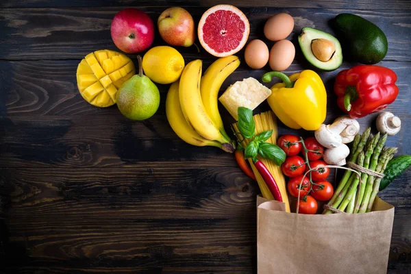Healthy food background. Healthy food in paper bag vegetables, fruits, pasta, eggs, cheese and mushrooms on dark. Shopping food supermarket concept. Vegetarian food. Top view. Copy space