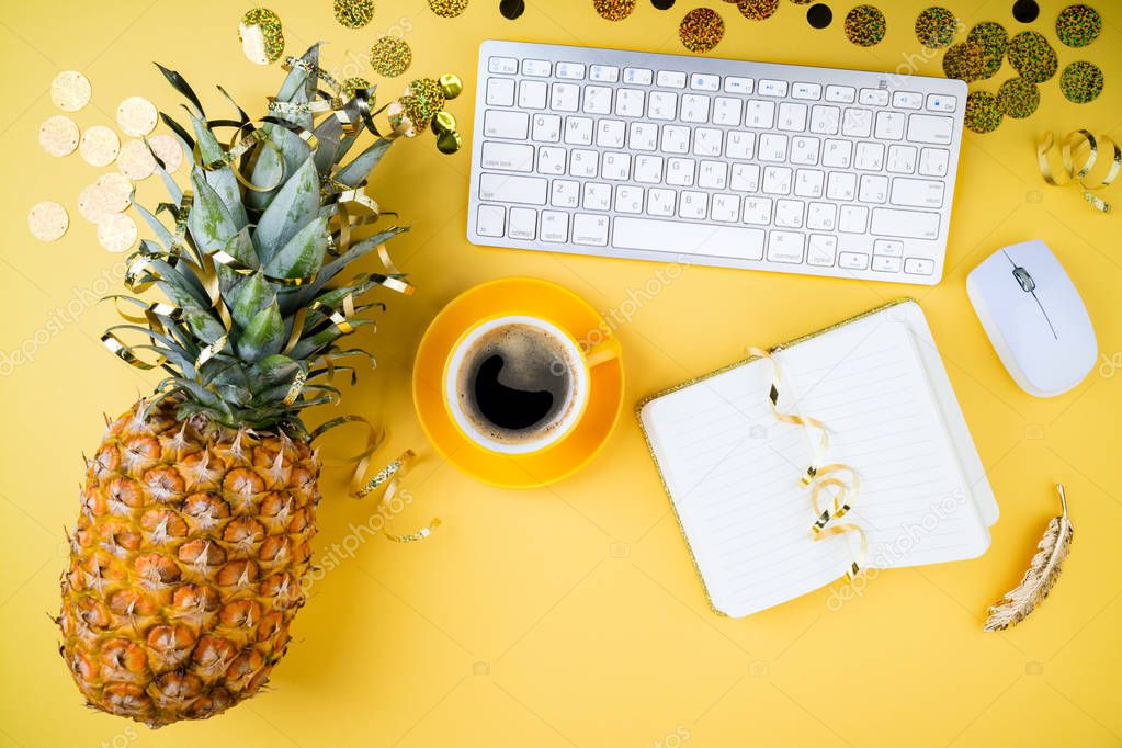 Fashion feminine home office, workspace flat lay. Pineapple, coffee cup, golden confetti, women's accessories and notebook on yellow table. Festive female background.  Top view