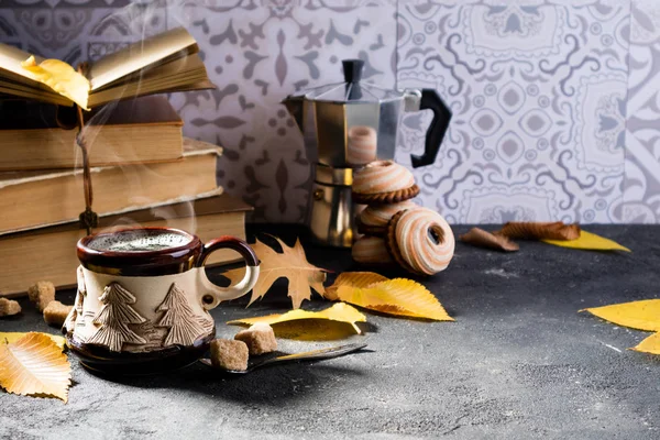 Autumn composition with coffee. Steaming coffee cup, autumn leaves, books, cookies and coffee pot. Autumn background with cozy home atmosphere