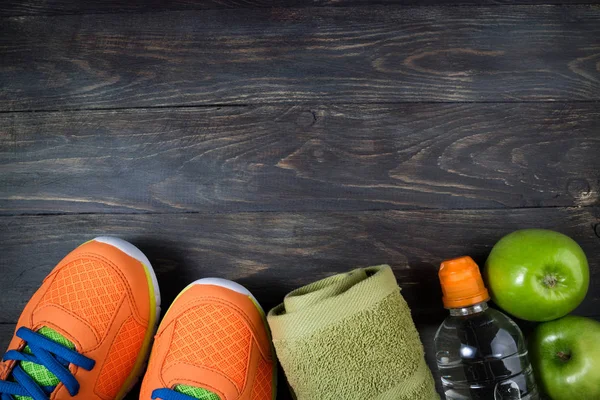Sport shoes, apple, bottle of water and towel on wooden backgrou