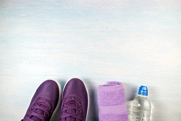 Sport shoes, bottle of water and towel on blue wooden background
