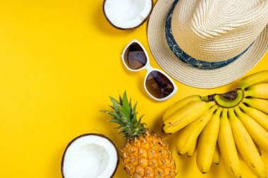 Yaz kadın moda plaj aksesuarları saman şapka, güneş gözlüğü ve sarı arka plan üzerinde tropikal meyveler. Yolculuk, meslekler, seyahat ve yaz dinlenme konsepti