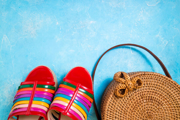 На голубом фоне лежали модные сумочки и яркие женские сандалии. Женские летние аксессуары. Летняя мода
