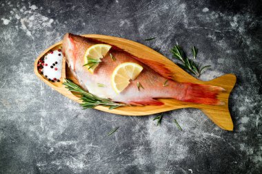 Limon dilimleri ile Balık çiğ snapper, otlar biberiye, tuz ve biber koyu arka plan üzerinde. Sağlıklı gıda ve diyet kavramı. Üstte görüntü