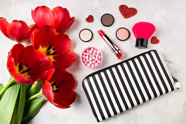 Fashion feminine background with makeup products, decorative cosmetics and tulip flowers on stone background. Fashion and beauty concept. Flat lay