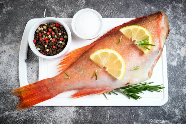 Pargo crudo de pescado con rodajas de limón, romero de hierbas, sal y pimienta sobre fondo oscuro. Comida saludable y concepto de dieta — Foto de Stock