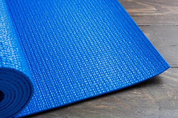 Blue yoga mat on wooden background. Equipment for yoga. Concept
