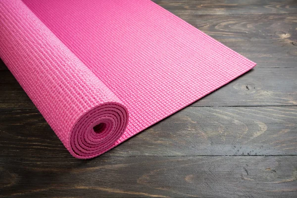 Pink yoga mat on wooden background. Equipment for yoga. Concept