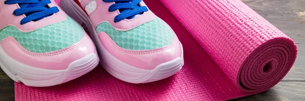 Pink yoga mat and sport shoes on wooden background. Healthy life