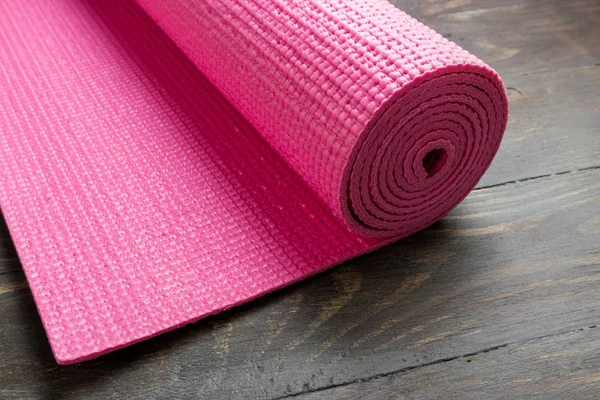 Розовый коврик для йоги на деревянном фоне. Оборудование для йоги. Концепция — стоковое фото