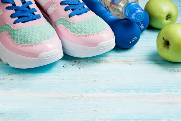Sapatos esportivos, halteres, garrafa de água, maçãs em backgrou azul — Fotografia de Stock