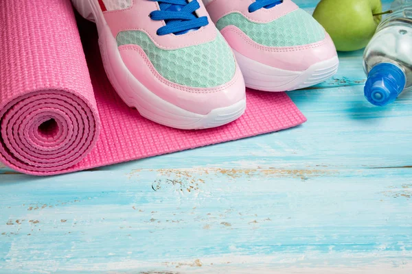 Rosa Yogamatte, Sportschuhe, Wasserflasche und Äpfel auf blauem Grund — Stockfoto