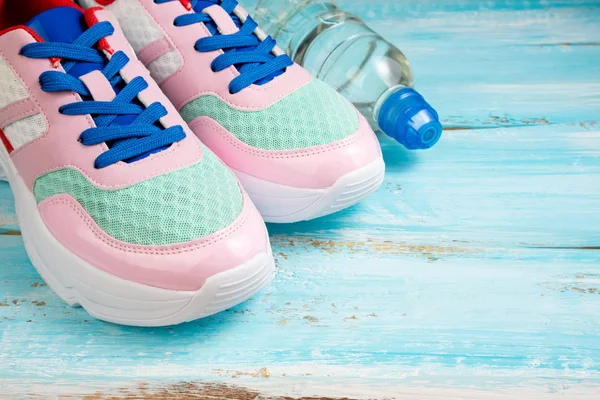 Zapatos deportivos rosa y botella de agua sobre fondo de madera azul . — Foto de Stock