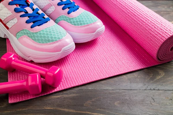 Pink yoga mat and sport shoes on wooden background. Healthy life