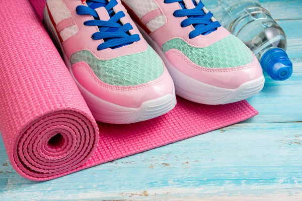 Pink yoga mat, sport shoes, bottle of water on blue wooden backg