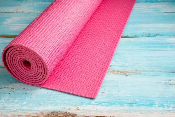 Pink yoga mat on blue wooden background. Equipment for yoga. Con