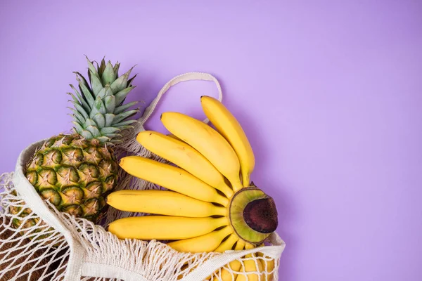 Shopping bag with organic banana and pineapple fruits on purple — Stock Photo, Image