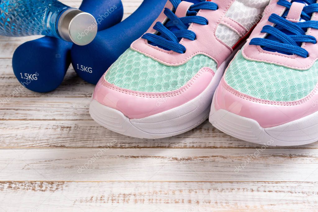 Sport shoes, dumbbells, bottle of water on wooden background. Sp