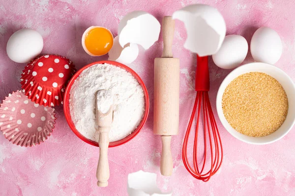 Ingredients for baking flour, eggs, sugar on pink background. Baking or cooking cakes or muffins. Baking background. Top view, flat lay