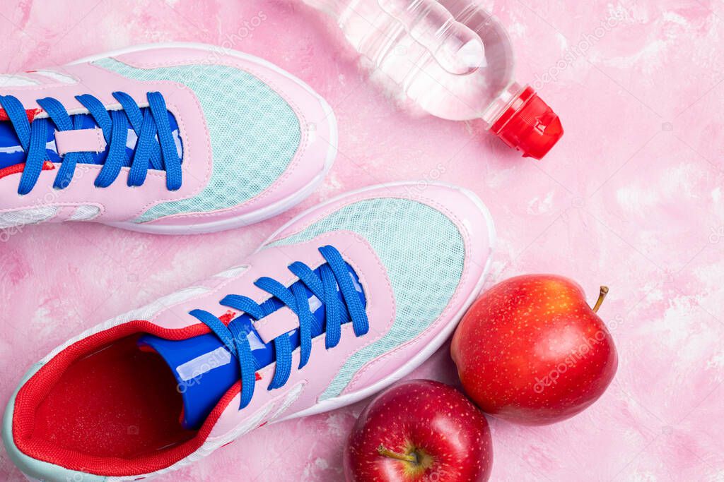Sport shoes, apple, bottle of water on pink background. Concept healthy lifestyle, active, healthy food, sport and diet. Sport equipment. Top view