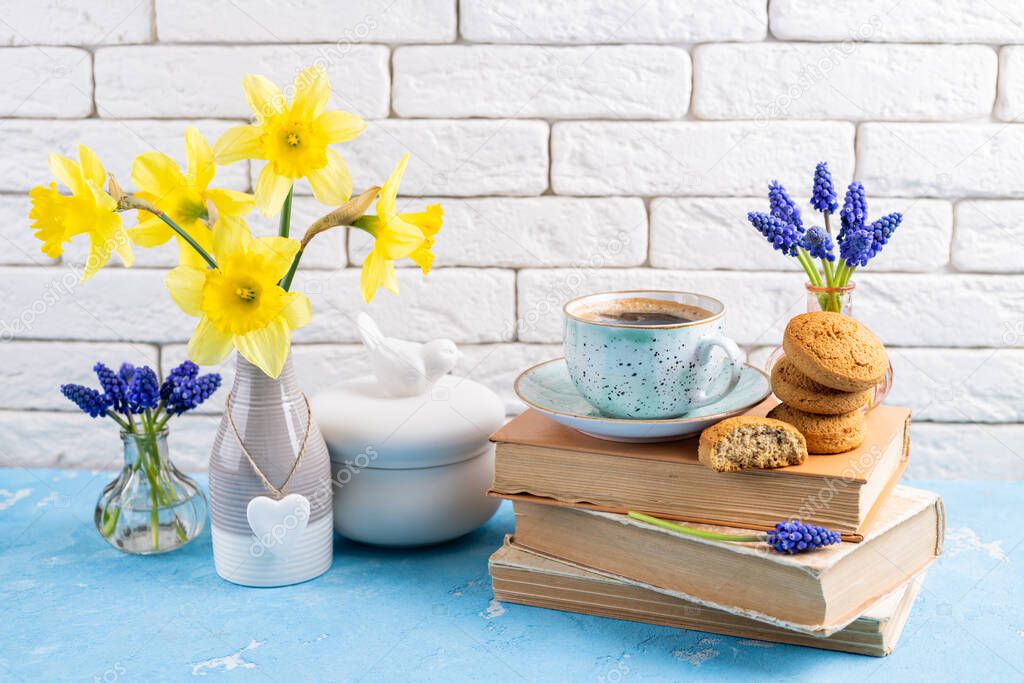 Bouquets of yellow daffodils flowers and grape hyacinth, coffee cup, books, cookies on table. Reading and breakfast. Concept stylish, hygge and cozy home interior