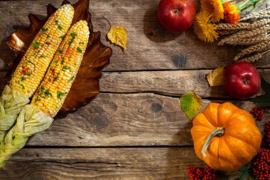 Şükran Günü için sonbahar geçmişi. Şükran Günü yemeği için sonbahar sofrası. Mısır, balkabağı, çiçek, meyve ve kırsal ahşap masa üzerindeki mevsimlik dekorasyonlarla dolu bir tabak. Boşluğu kopyala