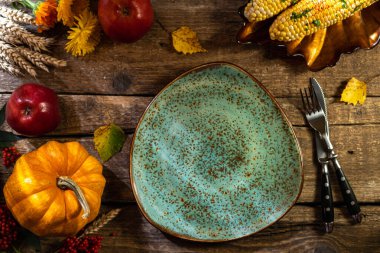 Şükran Günü geçmişi. Şükran Günü partisi ya da Şükran Günü yemeği için sonbahar sofrası. Tabak, çatal bıçak, balkabağı, mısır, çiçek, meyve ve kırsal ahşap masa üzerindeki mevsimlik dekorasyon