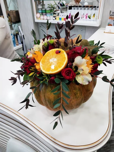 a bouquet of flowers and fruits in a pumpkin vase