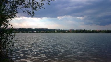 Zhuravlevka Gölü. Yaz ortası. Yakında gök gürültülü bir fırtına ve gerçek bir yaz yağmuru olacak. Bulutlar gökyüzünde toplanıyor. Gölün yüzeyi güneşte parlıyor. Dalgalar gümüş gibi görünüyor.!