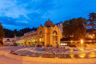 Tarihi Kolonada binasının manzarası ve Çek spa kasabası Marienbad 'daki şarkı söyleyen çeşme akşam alacakaranlığında.