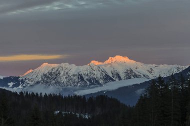 Akşam ışığında kürsü duvarından çekilen ve akşam güneşiyle aydınlatılan zirve, 2013 kışında vadide kükreyen ve sisli peçeler.