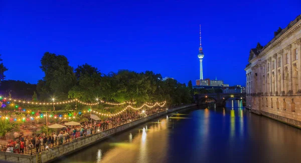 Berlin televizyon kulesine ve nehir kıyısındaki açık hava bira bahçesine bakın. Akşam alacakaranlığı boyunca Spree Nehri.