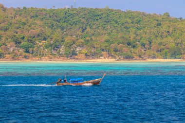Arka planda tropik ada ve plajla yelken açarken tipik bir uzun kuyruklu teknenin fotoğrafı Kasım 2013 'te Tayland' da öğleden sonra bulutsuz gökyüzünde çekildi.