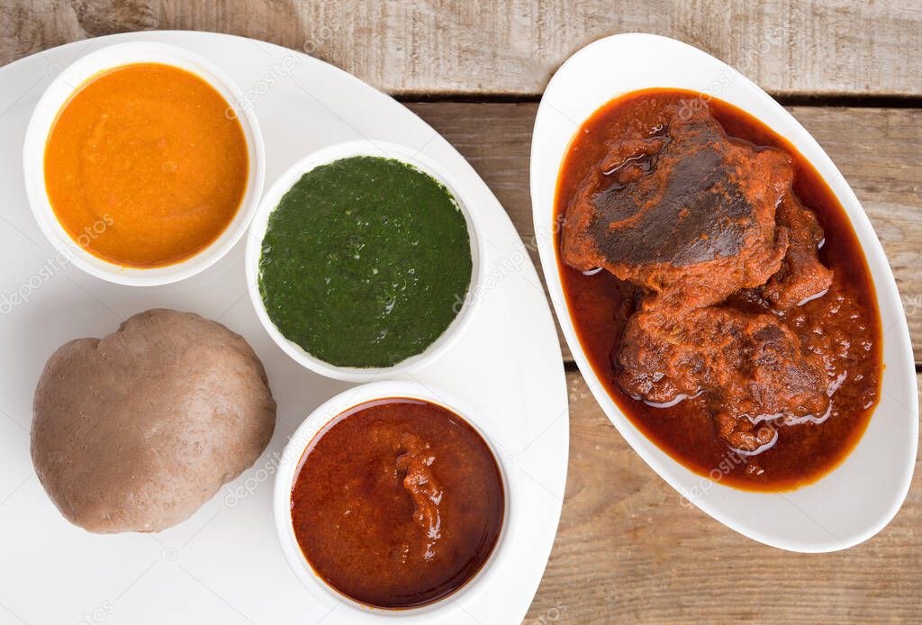 Top view of a meal of Nigerian Amala, Ewedu and Gbegiri Soup Served with Goat Meat Stew in a white bowl and white tray on a wooden table