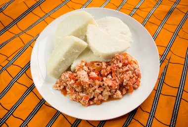 Lezzetli haşlanmış tatlı patates ve çırpılmış yumurta. Renkli turuncu çizgili masa örtüsünde beyaz bir tabakta servis ediliyor.