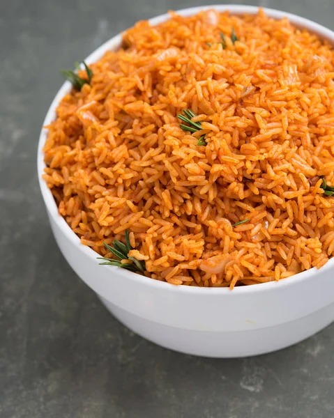 Büyük beyaz bir kase lezzetli Nijerya Jollof Rice yeşil baharatlarla süslenmiş.