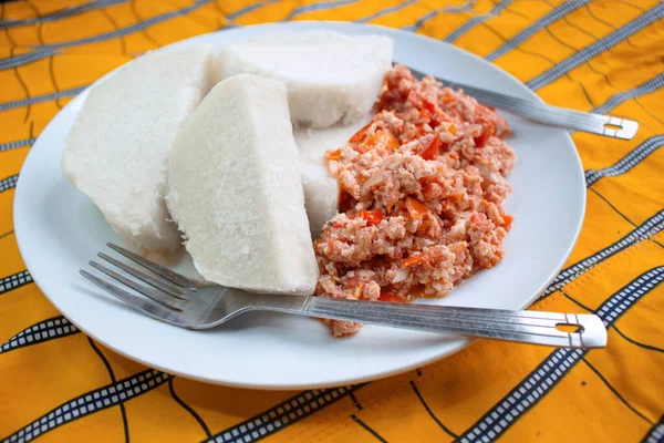 Kaynamış yer elması ve lezzetli omlet, beyaz bir tabakta servis ediliyor. Renkli turuncu çizgili masa örtüsü, yanında çatal ve bıçak var.