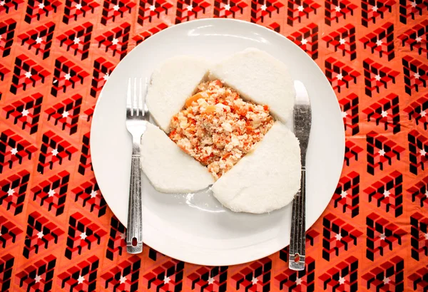 Haşlanmış tatlı patates ve dilimlenmiş soğan, domates ve kırmızı biberle hazırlanmış omlet. Renkli kırmızı bir masa örtüsü üzerinde servis edilmiş, yanına çatal ve bıçak yerleştirilmiş.