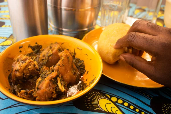 Renkli mavi ve sarı Afrika desenli masa örtüsüne sarılı çeşitli et ve balıklar içeren kalın Nijerya sebze çorbası ile portakal kasesinden veya Garri 'den yemek.