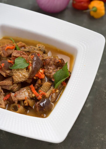 Tasty Nigerian goat meat pepper soup garnished with sliced pepper in a white bowl