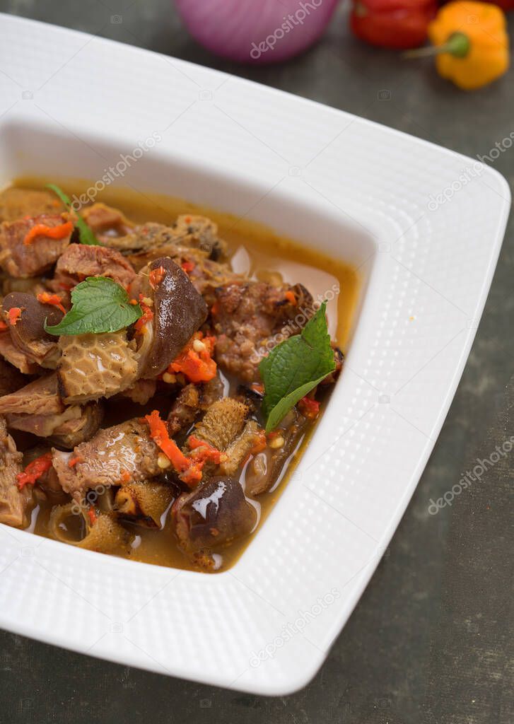 Tasty Nigerian goat meat pepper soup garnished with sliced pepper in a white bowl 