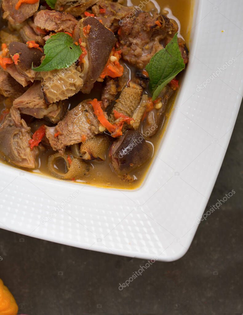 Partial view of a bowl of hot spicy Nigerian goat meat pepper soup. Served in a white bowl on a dark table
