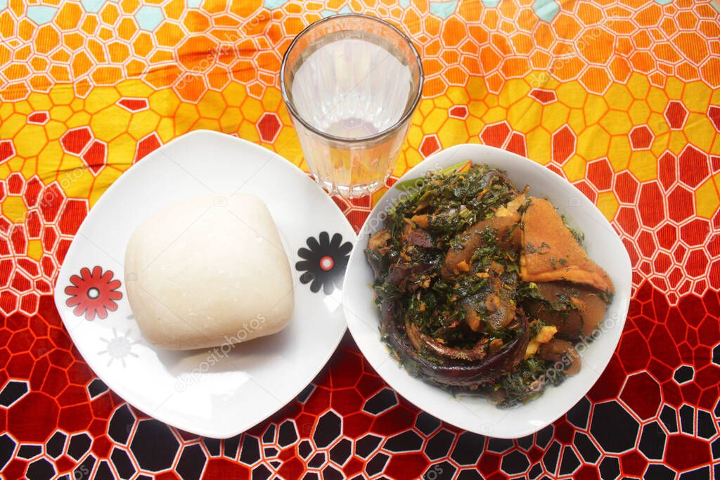Top view of a served dish of pounded yam and thick vegetable soup cooked with dried fish, kpomo, shaki and crayfish. This is a traditional Nigerian meal