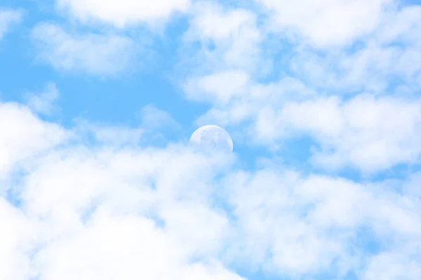 Mavi gökyüzü ve bulutlarla gündüz vakti yarım ay.