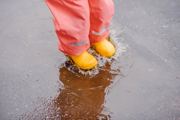 happy baby girl with an umbrella in the rain runs through the puddles playing outdoors