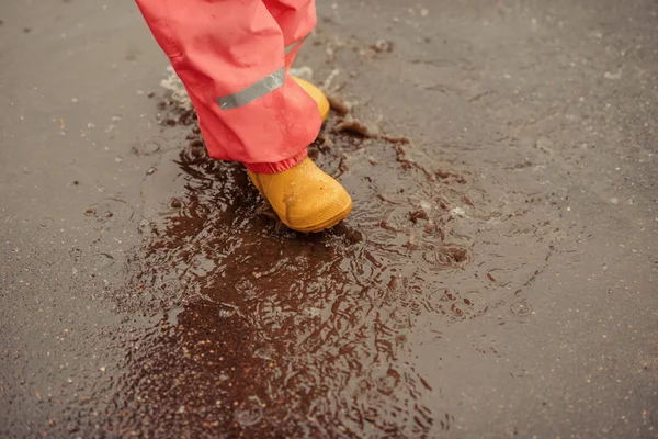 happy baby girl with an umbrella in the rain runs through the puddles playing outdoors