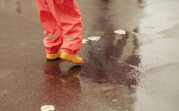 happy baby girl with an umbrella in the rain runs through the puddles playing outdoors