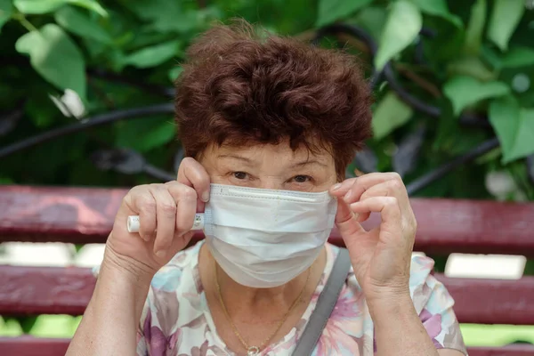 Woman wearing surgical mask epidemic prevention covering face. Senior woman in late 60s using mask looking to camera.